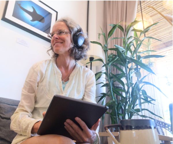 Ann-Mari med hörlurar och surfplatta med växt bakom, i samtal
